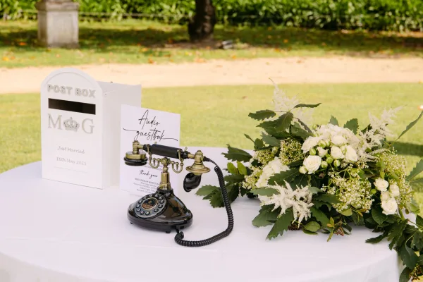 Wedding guestbook table with audio guestbook wedding sign and vintage rotary phone, white post box, and greenery garland on a garden lawn