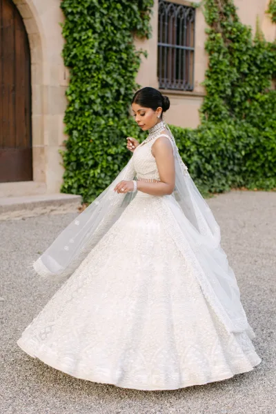Bridal portrait of a bride in a ball gown wedding dress, holding her cathedral veil, beside an ivy-covered stone building doorway