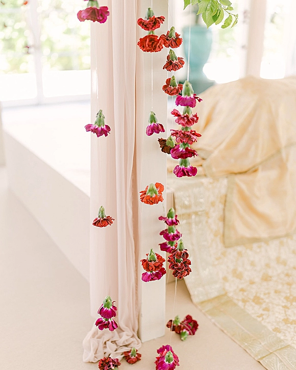 Hanging flower decor with vertical floral garland strands and soft blush fabric draping, lit by window light over an indoor seating area