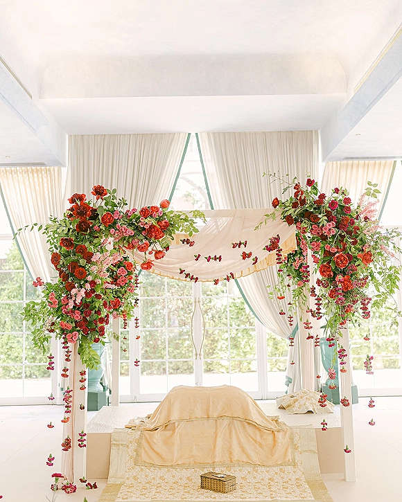 Wedding mandap decor with an indian wedding mandap canopy, draped fabric and hanging flower garlands above platform seating in an indoor hall