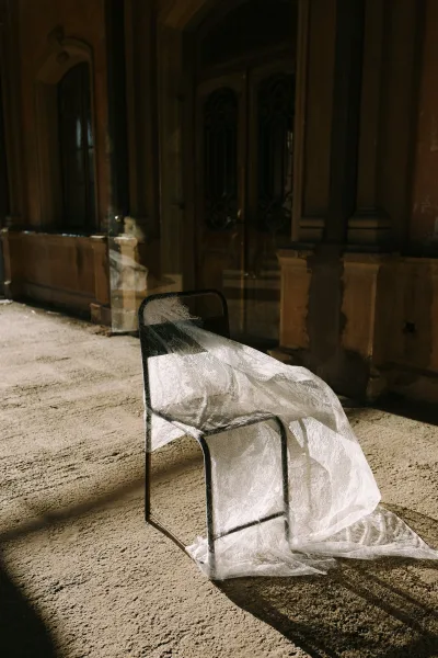 Bridal veil detail with lace wedding veil draped over a chair, scalloped edge on stone floor in a shadowed arched hallway