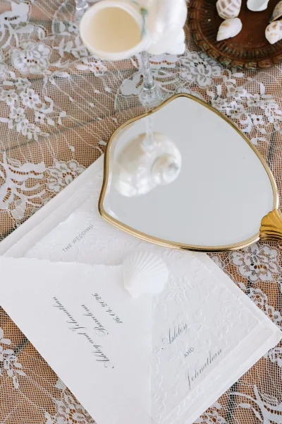 Invitation suite with wedding invitation suite details, embossed calligraphy cards and envelopes arranged on a lace tablecloth on wood tabletop