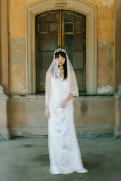 Bridal portrait of a bride in a tiara wedding veil, wearing a strapless dress with lace veil, posed by an arched doorway and weathered wall