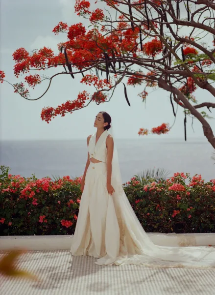 Bridal portrait of a bride under a flowering tree with a long veil, framed by bougainvillea on a terrace above the ocean.