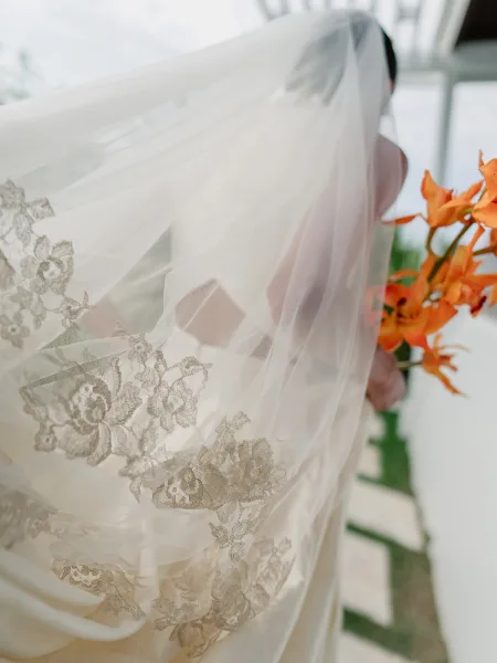 Lace wedding veil, a lace applique veil draping softly over a bridal gown beneath pergola beams against the sky.