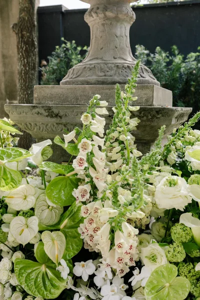Wedding flower arrangement of white and green wedding flowers displayed in a stone urn against a dark wall.