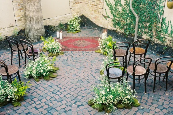 Ceremony setup with intimate ceremony seating centered on a vintage rug, framed by brick pavers and an ivy-draped wall.