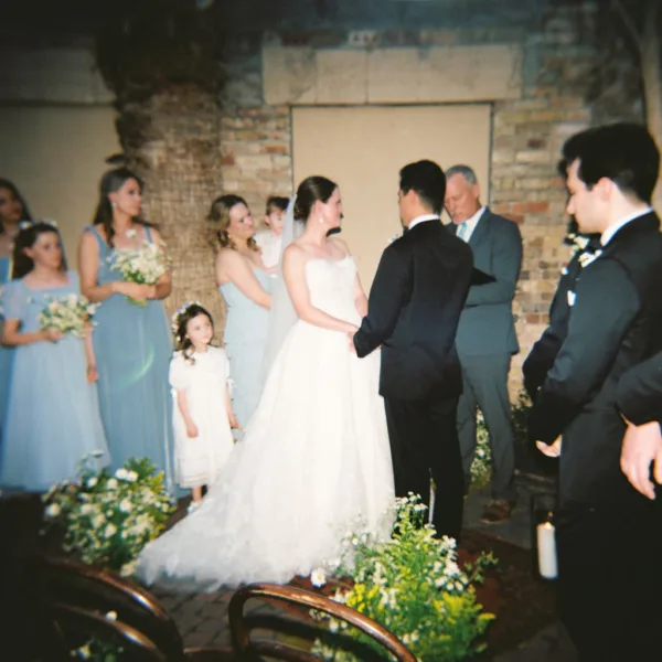 Ceremony moment with the couple holding hands beneath a stone arch, the bride’s veil trailing as the wedding party lines the aisle.