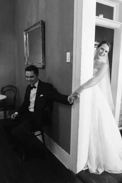 First touch moment captures a no first look idea as the couple's hands meet around a doorway, her veil brushing the frame in a quiet pause.