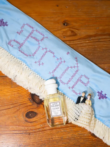 Bridal perfume, the wedding day scent, styled in a flat lay beside an embroidered bride sash, presented as bridal styling details.