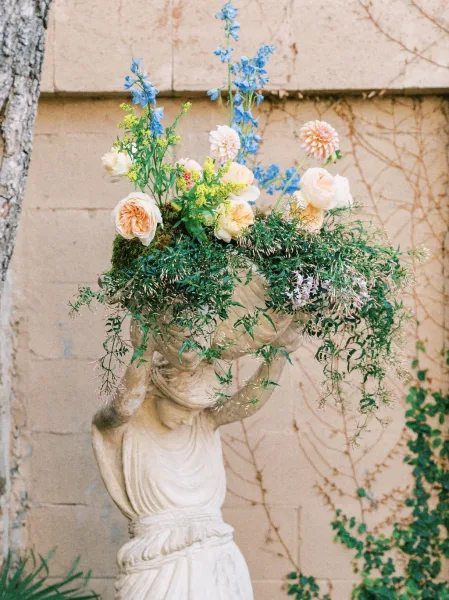 Wedding flower arrangement showcasing a garden rose arrangement styled in a classical urn against a stucco wall draped with climbing vines.