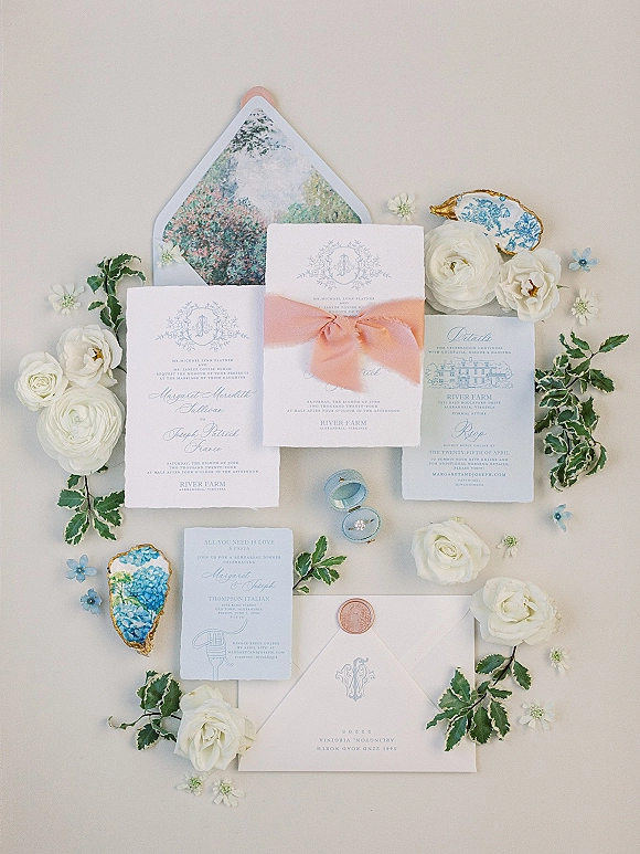 Invitation suite wedding invitation flat lay with ribbon bow, wax-sealed envelope, ring box and engagement ring, white roses and oyster shells on neutral surface