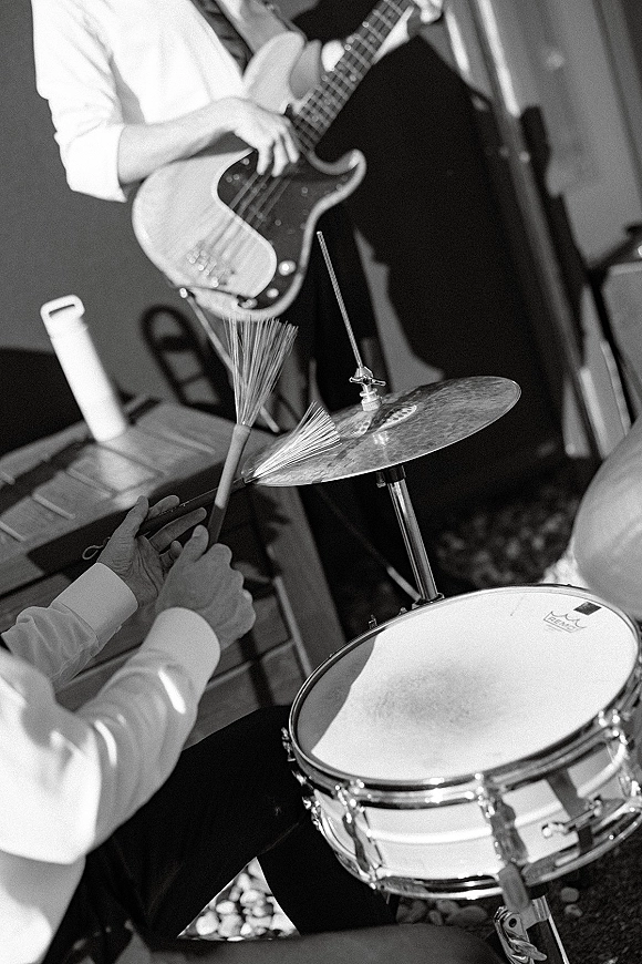 Wedding band playing live wedding music with a drummer using brushes on snare and cymbal beside an electric bass in an indoor corner