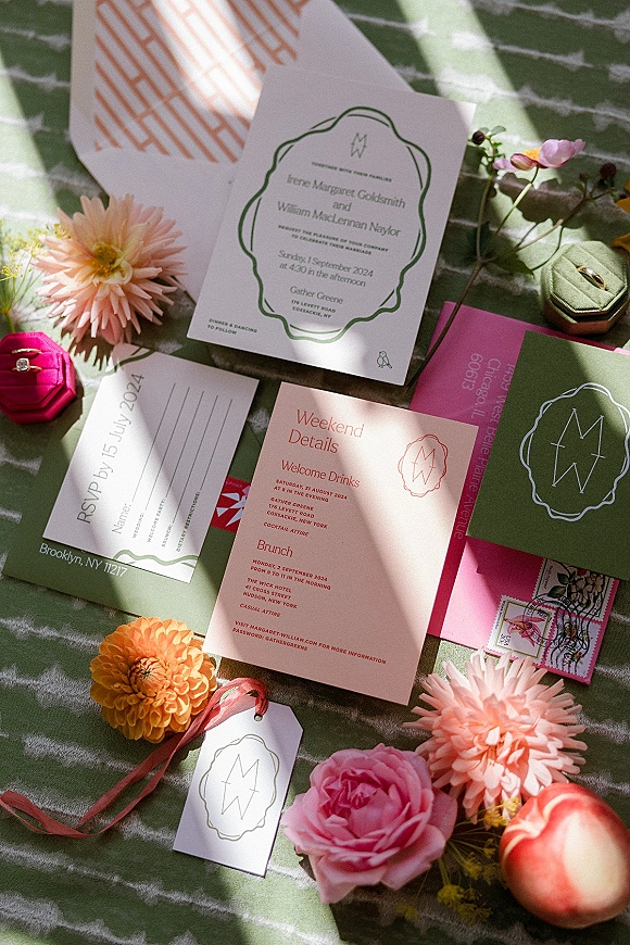 Invitation suite with colorful wedding invitations, RSVP and weekend details cards, wax seal, vintage postage, florals, and ring box on striped fabric in sunlit shadows