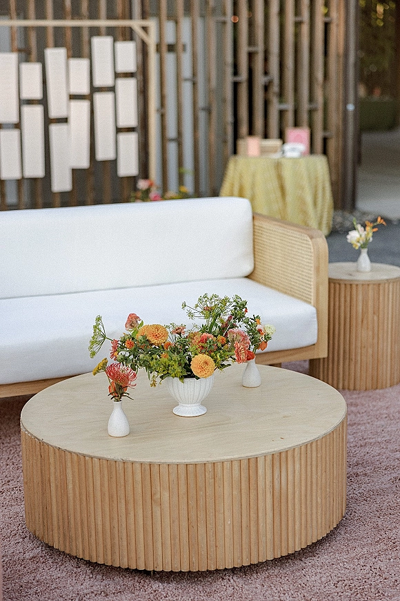 Lounge seating area with wedding lounge furniture, a white upholstered sofa and wooden coffee table, plus floral centerpiece by hanging escort cards on a wood slat wall