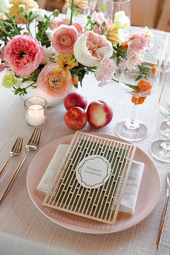 Reception tablescape with wedding place setting, pastel floral centerpiece, peaches, votive candle, wine glasses, and blush plate with menu card