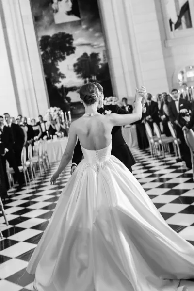 First dance as bride and groom dancing on a black and white checkered floor, her strapless satin ball gown twirling in a grand ballroom