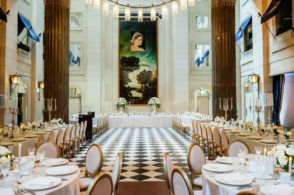 Wedding reception decor with long banquet table wedding setup, white linens, floral centerpieces and tall candelabras in a grand hall with checkered floor