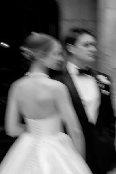 Couple portrait in a black and white wedding portrait style, bride and groom walking with motion blur past a stone wall doorway