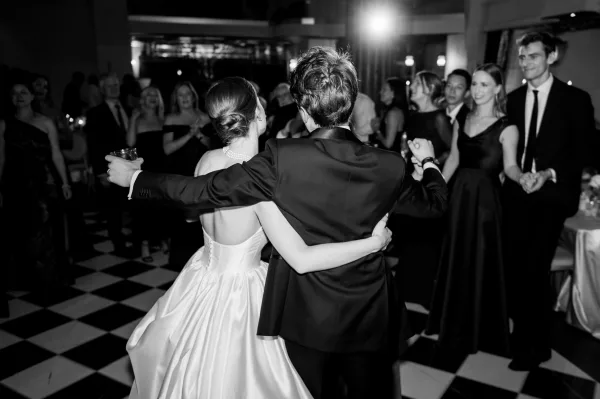 Wedding reception dancing as bride in strapless dress and groom in tuxedo share a first dance on a checkered floor, guests watching nearby