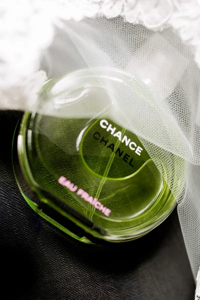 Wedding perfume detail with a green bridal perfume bottle draped in lace veil on dark fabric, soft tulle folds highlighting luxury prep styling