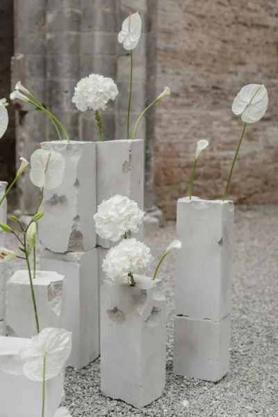 Wedding floral installation with minimalist wedding flowers, white anthurium and calla lilies on concrete pedestals in a stone courtyard