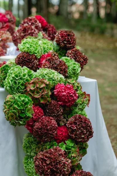 Wedding floral arrangement with hydrangea wedding centerpiece on a white tablecloth, set outdoors with trees and a grassy lawn in back