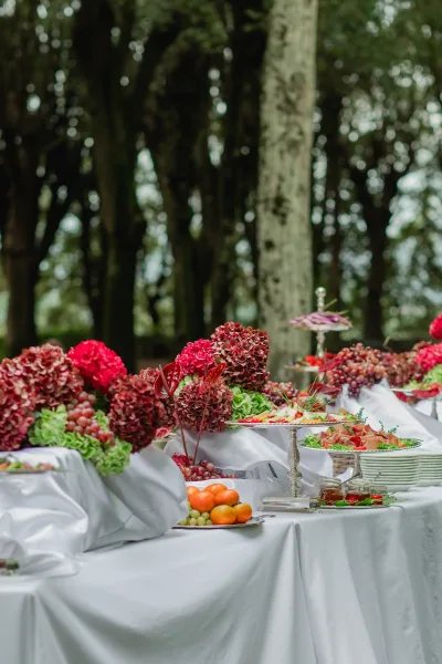 Wedding buffet table with grapes, citrus, charcuterie and cheese on silver trays, framed by hydrangea accent in a forest setting