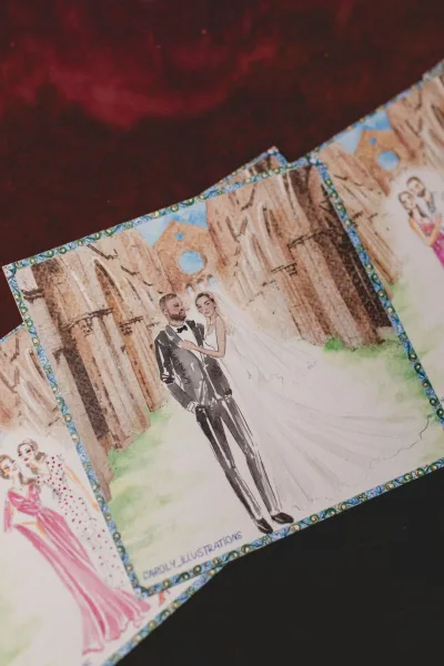 Wedding invitation with custom wedding illustration of an illustrated couple, watercolor artwork and patterned border, on stacked cards on a dark tabletop