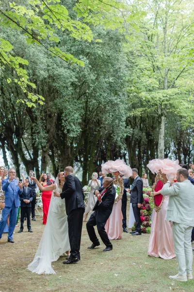 Wedding recessional as newlyweds walk down the aisle kissing, veil flowing, guests cheering with phones in a garden setting