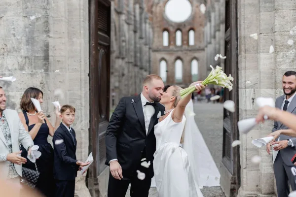 Wedding kiss as the newlyweds kissing under a stone archway, confetti flying, bride in veil holding bouquet beside groom in tuxedo