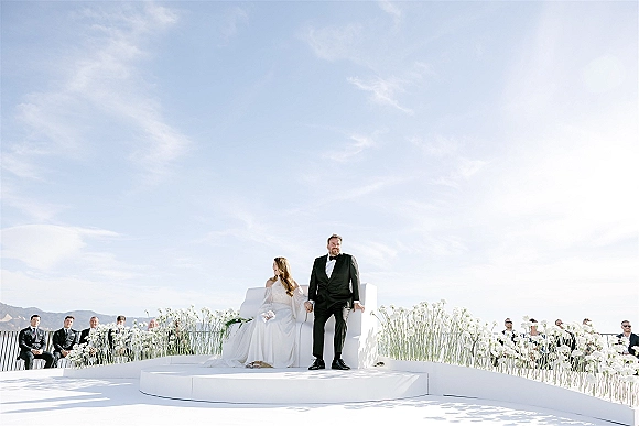 Ceremony moment at an outdoor wedding ceremony with bride in strapless dress and groom in tux on a white stage, mountains beyond