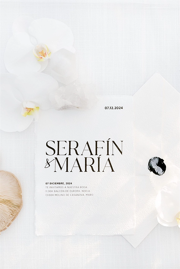 Wedding invitation suite with minimalist wedding invitations, envelopes and black wax seal, styled with white orchids and a seashell on linen