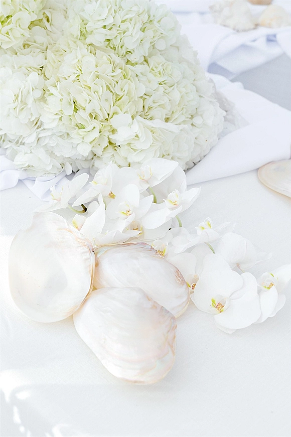Wedding bouquet of white hydrangea blooms with cascading orchids and anthurium, tied with ribbon on crisp white linens flat lay