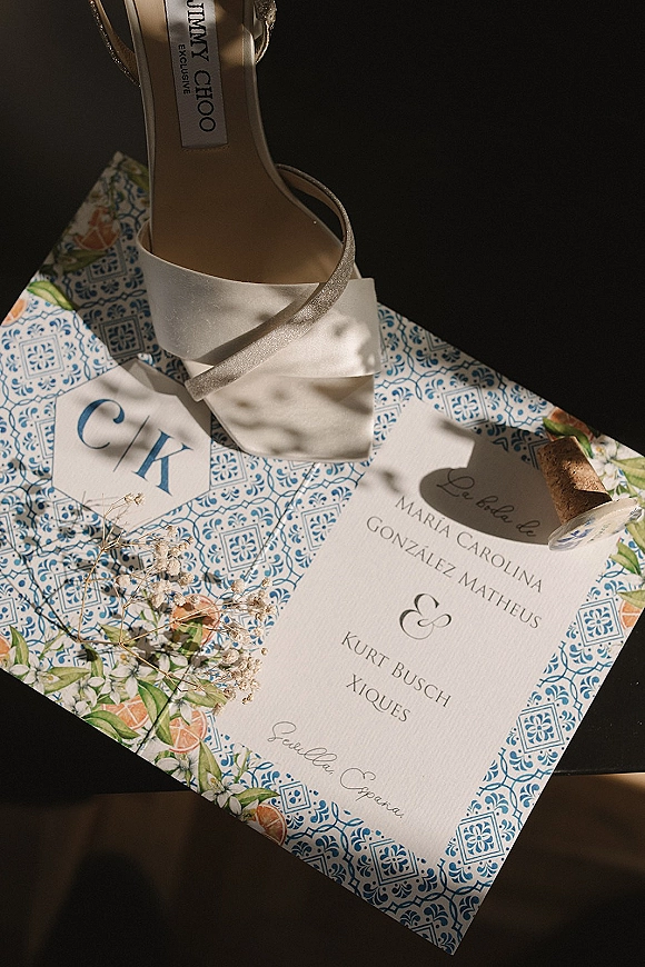 Invitation suite flat lay with patterned cards, monogram and place card, plus dried flowers and cork detail on a dark surface with shadows