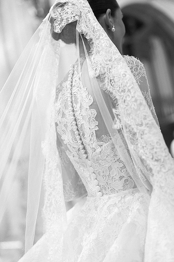 Bridal veil draped over a bridal updo, lace wedding veil framing a button-back lace dress with pearl jewelry in an indoor venue