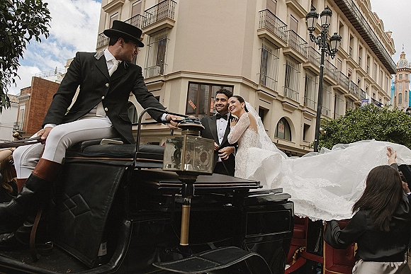 Wedding couple portrait of bride and groom in carriage, her lace veil and dress beside his tuxedo, on a city street by historic balconies