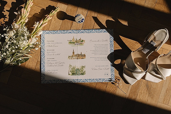 Wedding invitation suite with blue and white wedding invitations, wax seal, bridal shoes and baby's breath bouquet on wood parquet in window light