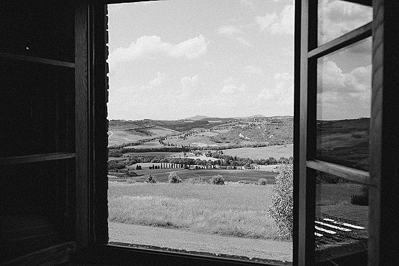 Outdoor ceremony site with wedding ceremony chairs arranged on grass, framed by an open window view of rolling hills and cypress trees