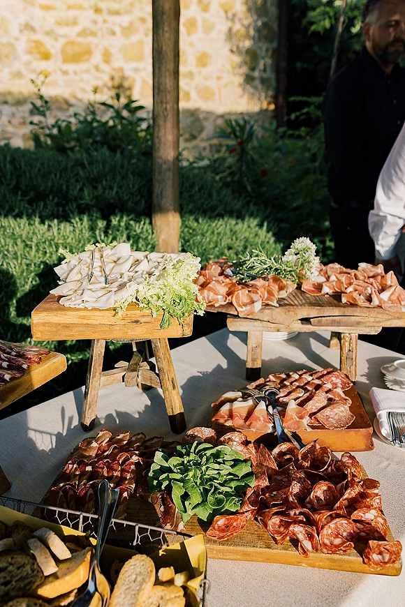 Wedding charcuterie table with cured meats, cheese slices and bread on wood boards, lettuce garnish and herbs in a garden setting