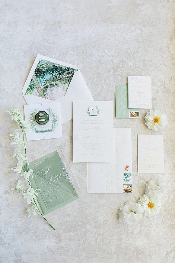 Invitation suite wedding invitation flat lay with envelopes, RSVP card, stamps, and engagement rings on a light stone surface with white flowers