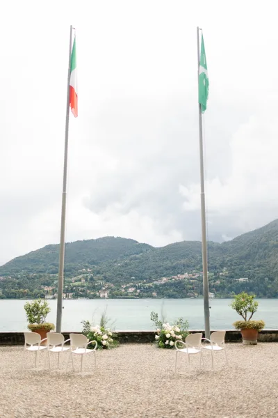Ceremony setup with outdoor ceremony chairs lined on gravel, framed by ground florals and potted trees overlooking a lake and mountains
