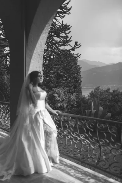 Bridal portrait of a bride in a strapless wedding dress holding her veil on a balcony, with mountains and a lake beyond columns