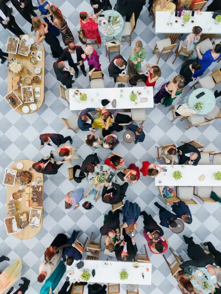 Wedding cocktail hour overhead view with guests mingling around cocktail tables, buffet desserts and drinks on a checkered tile floor indoors