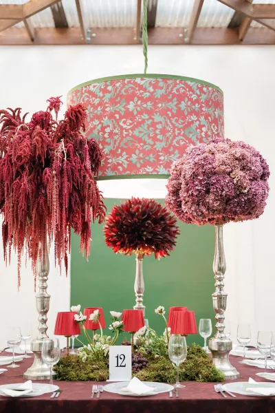 Reception tablescape with wedding table centerpieces in silver pedestal vases, burgundy linen, moss runner, grapes, and a patterned drum chandelier overhead