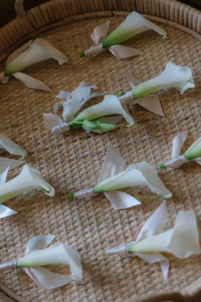 Calla lily boutonnieres with white calla lilies wrapped in satin ribbon and floral tape, arranged in a flat lay on a wicker tray
