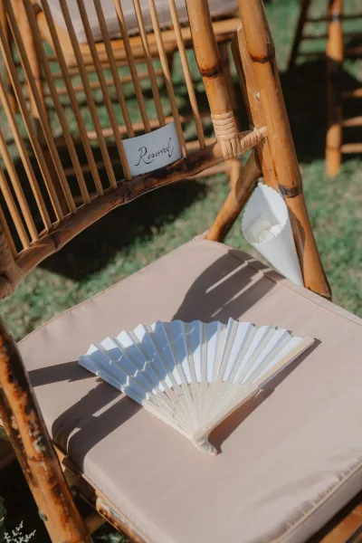 Ceremony chair decor with reserved sign on chair, bamboo chair cushion, petal cone and folding fan on a sunny grass lawn