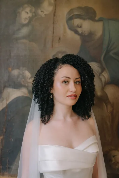 Bridal portrait of a bride in a strapless wedding dress with veil and drop earrings, posing before a painted mural wall indoors