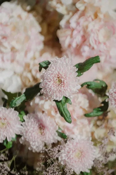 Wedding florals with blush wedding flowers and pink chrysanthemums, layered greenery leaves against a soft blurred floral backdrop