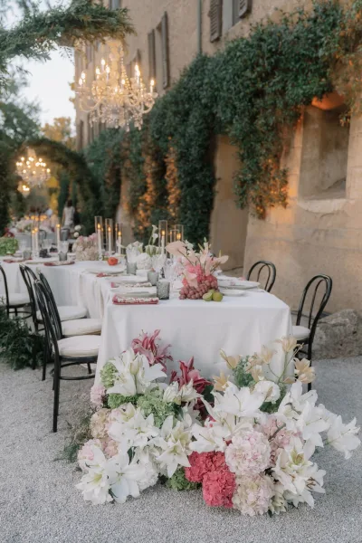 Reception tablescape at an outdoor wedding reception with white linens, black bistro chairs, taper candles, florals, and ivy wall backdrop